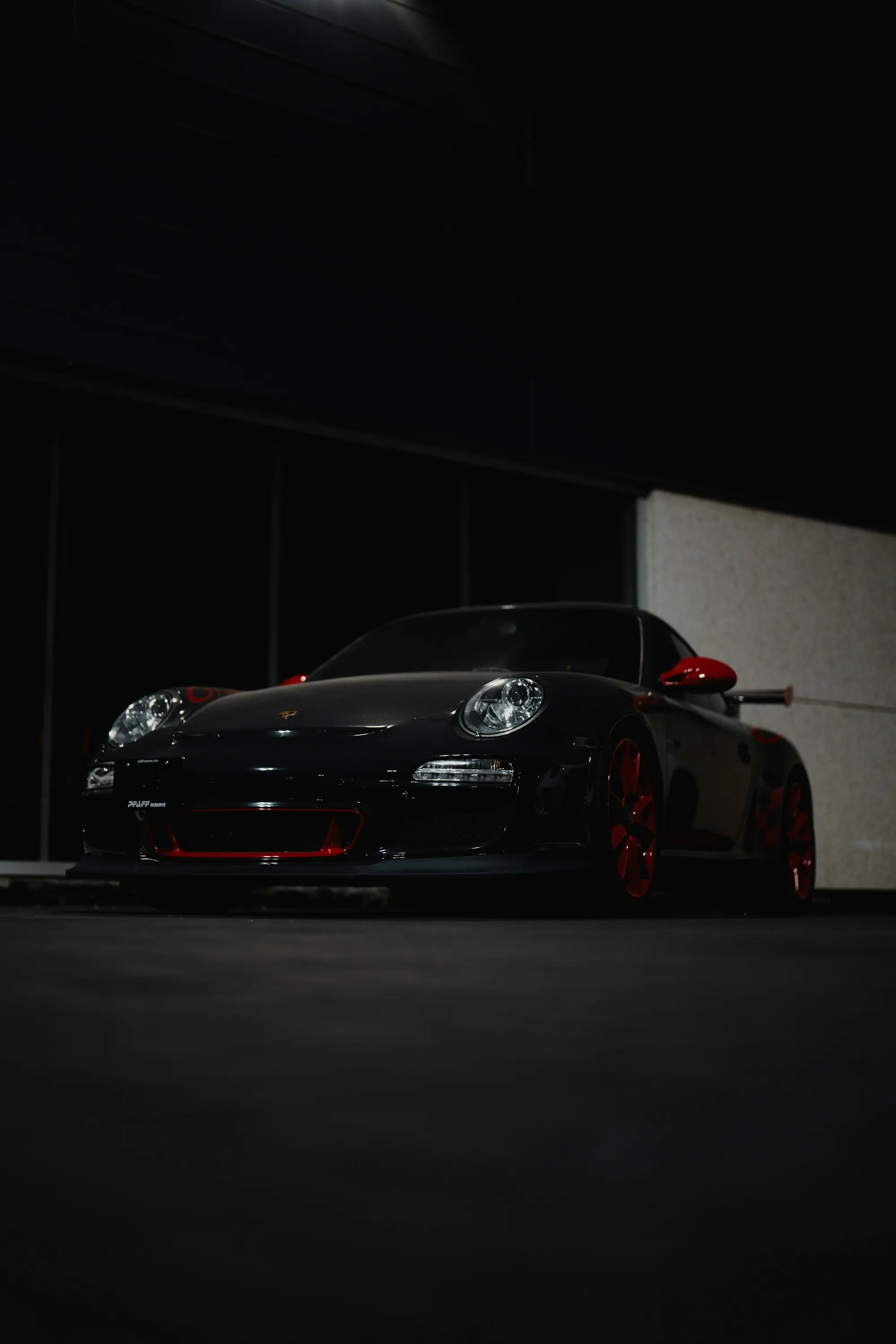 A black Porsche 911 GT3 RS with red wheels, lit low in a darkened building